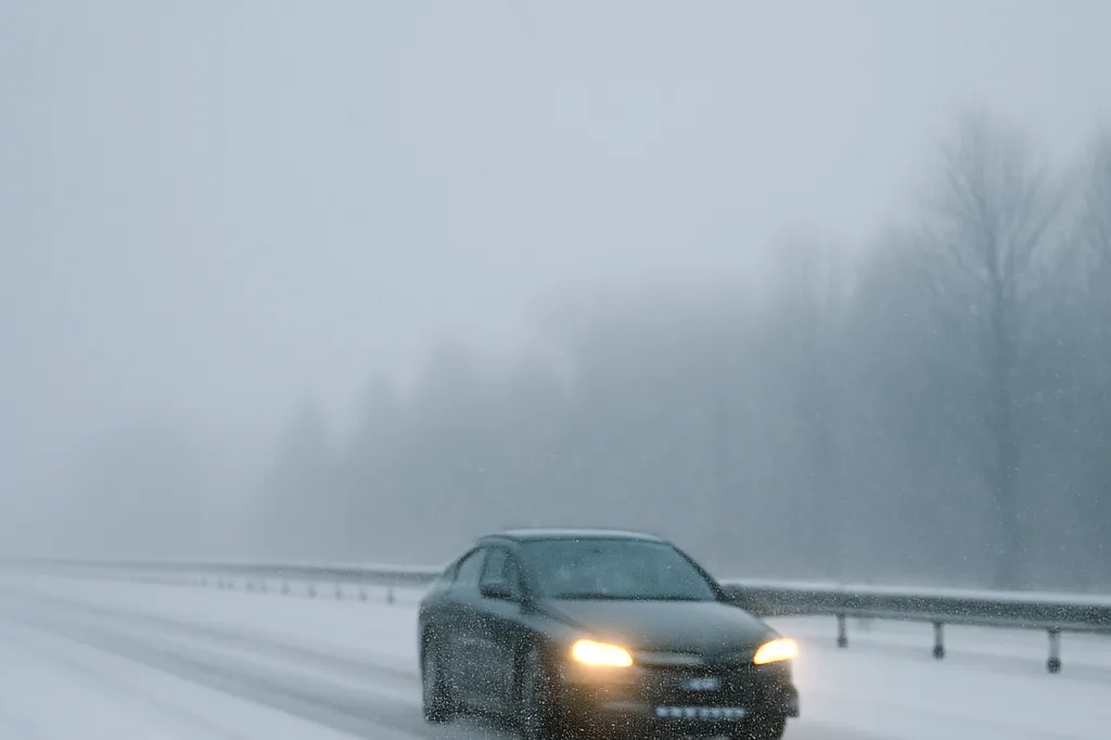 A car driving cautiously on a snow-covered highway near Ottawa with reduced visibility