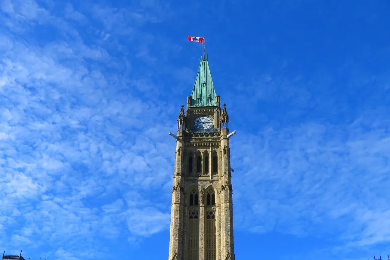 The Peace Tower's clock face and copper-green spire against a clear blue sky, flag flying at the top